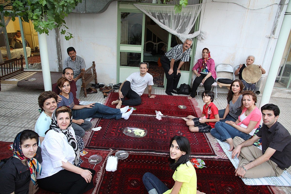 iranian family group seated on carpets outside a home, sharing snacks