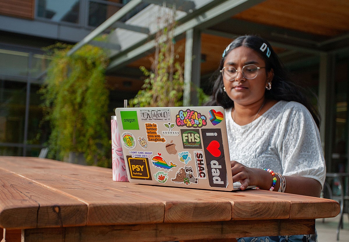 student at campus picnic table working on laptop covered in colorful stickers with positive messages