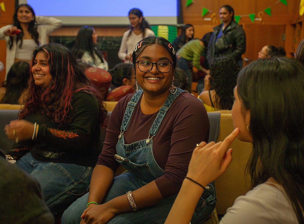 student smiling at another student in a crowded, lively room of students engaging with one another