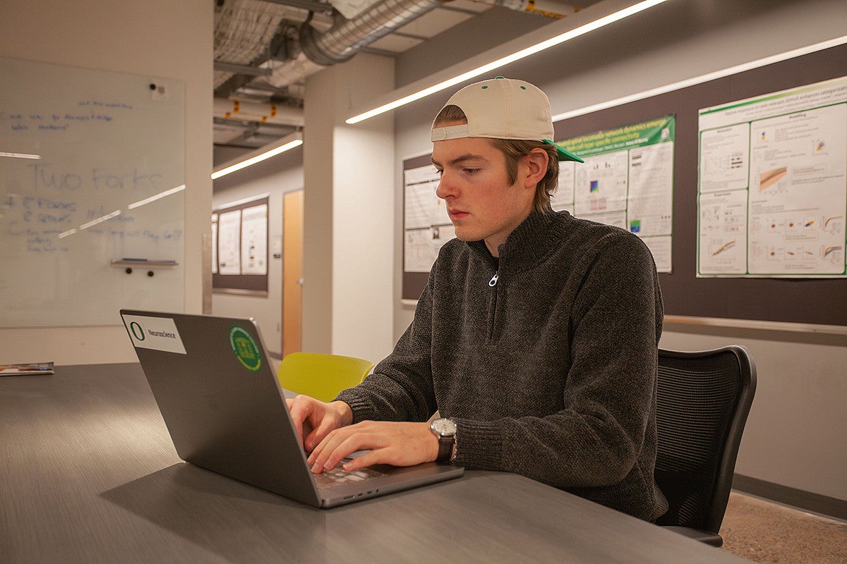 student seated at table in science building, working on laptop