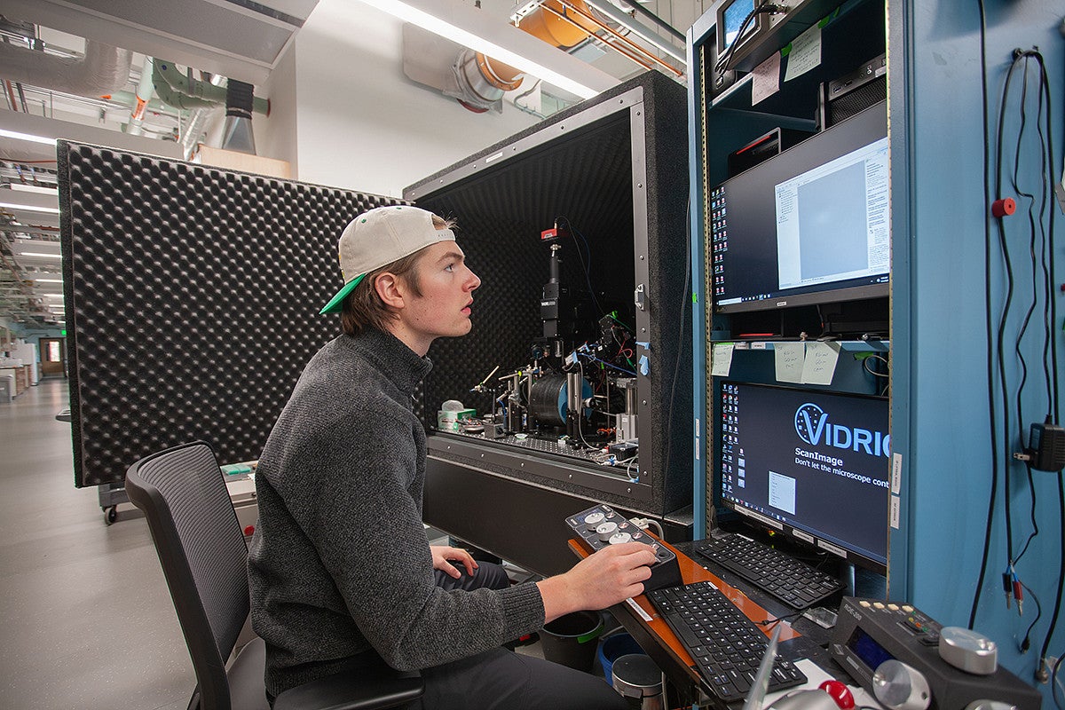 student seated at a large piece of science equipment, typing on a keyboard and reading a screen