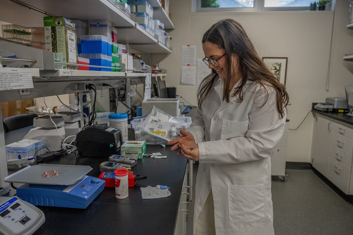 person in lab pricking their finger to take a blood sample
