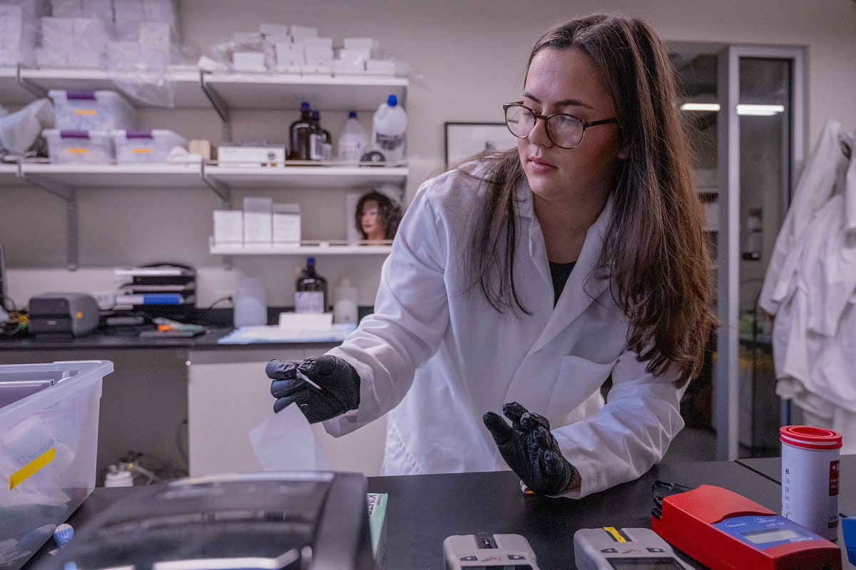 student at lab bench in white coat, working with blood samples