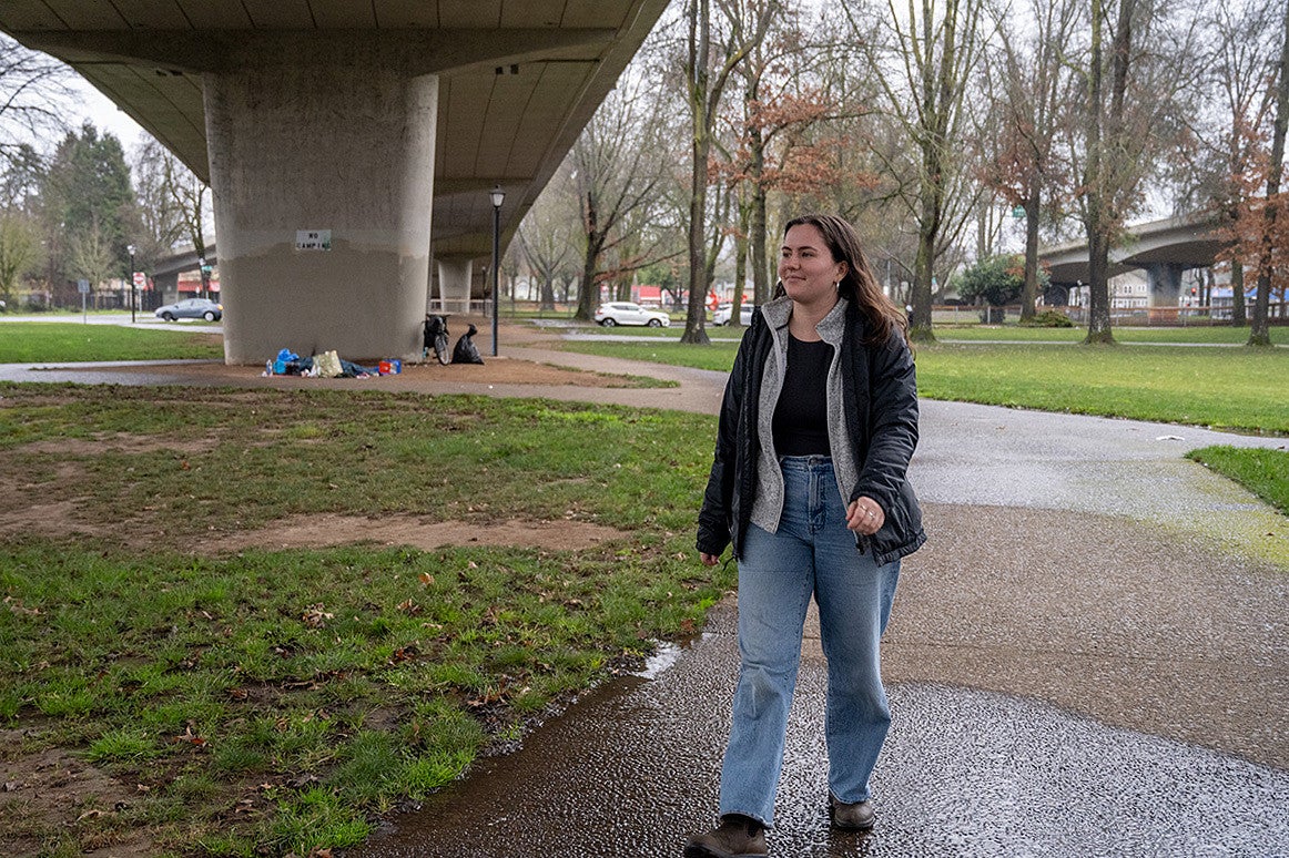 person walking through a park under a highway on a rainy day