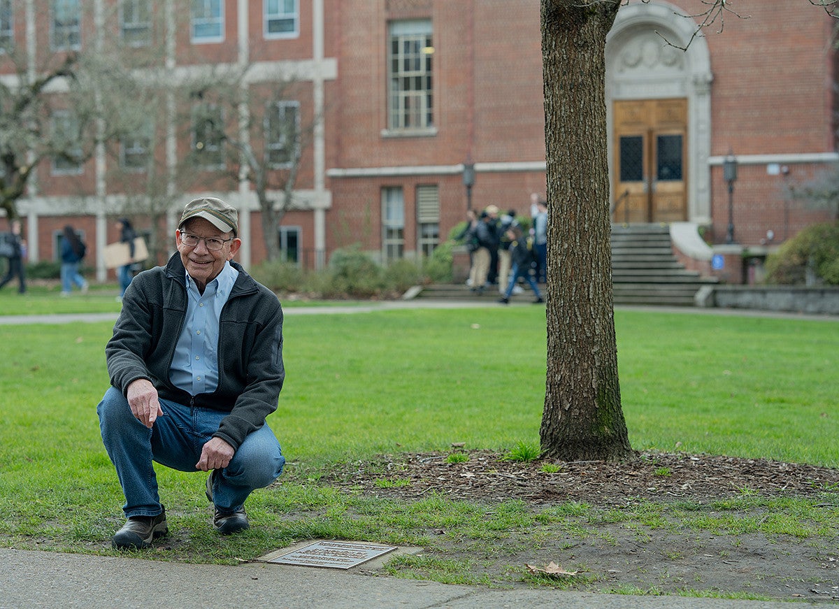 peter defazio kneeling next to a plaque and tree named in his honor across the memorial quad from Chapman Hall