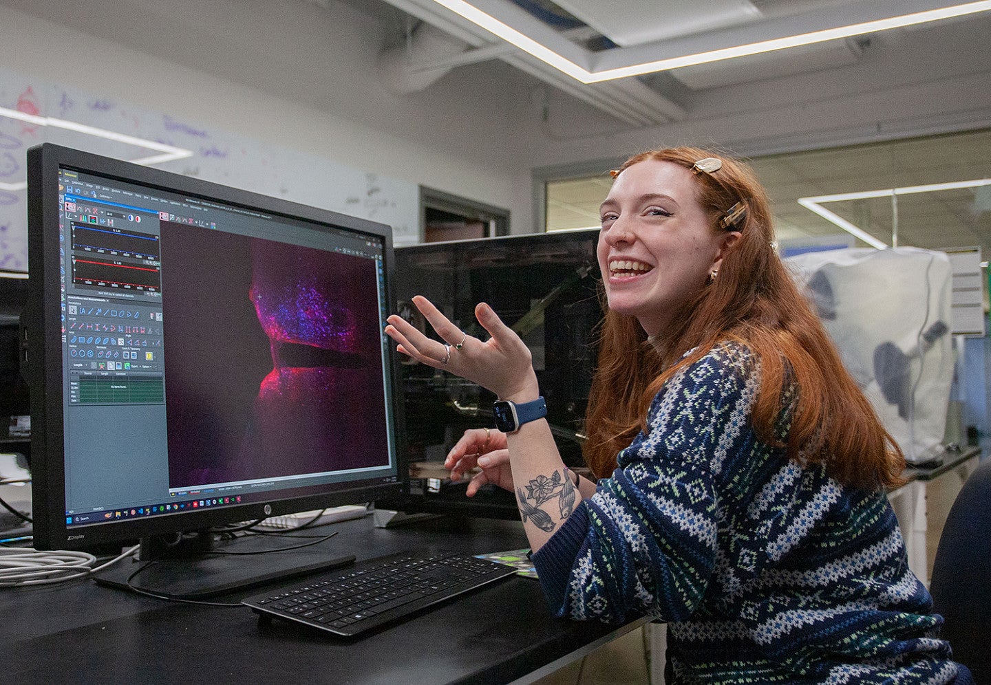 avery suriano laughing while seated at lab computer with colorful science image on screen