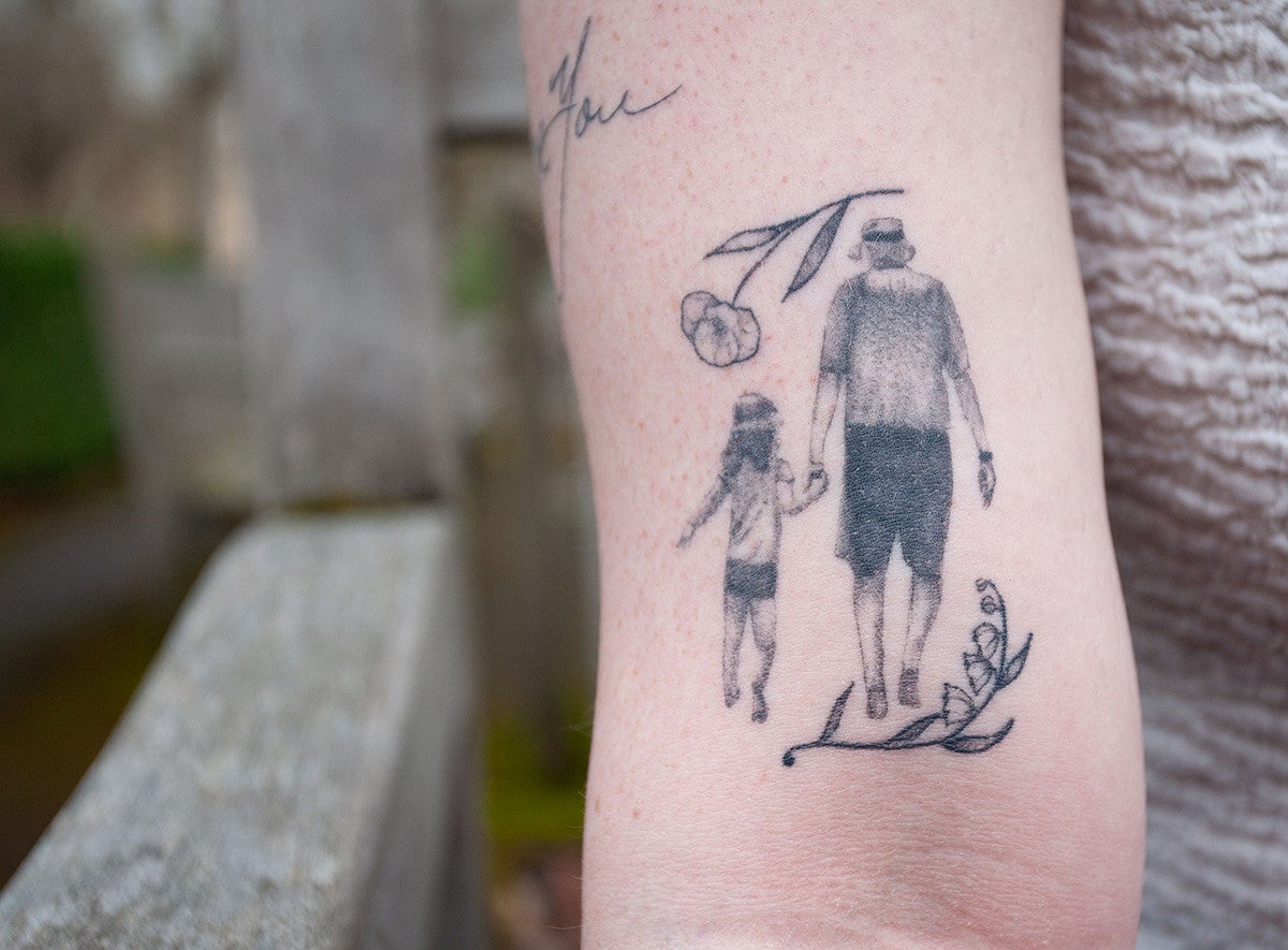 closeup of a tattoo above elbow, showing a man walking hand in hand with a girl, from behind, framed by flowers