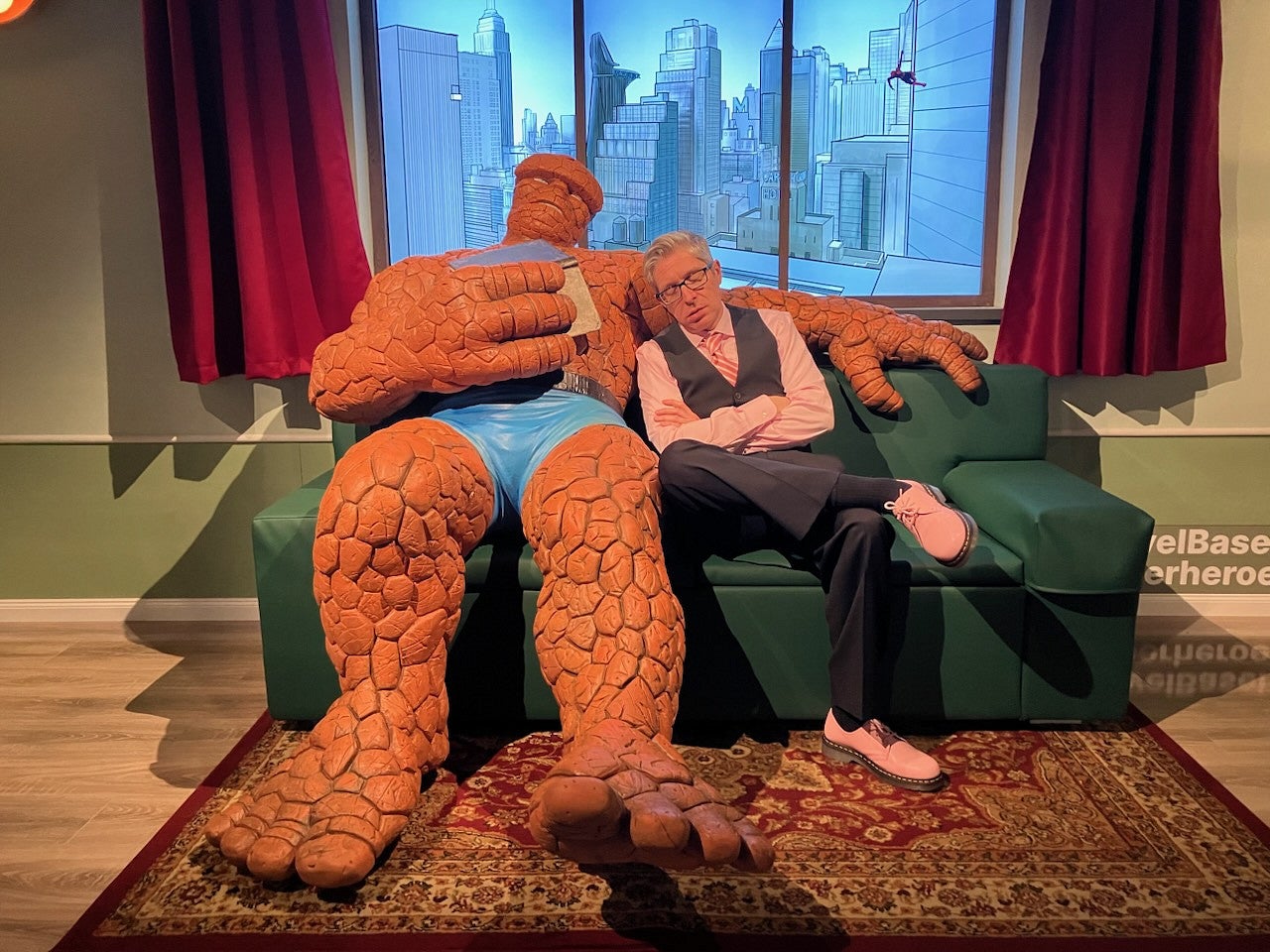 ben saunders pretending to sleep on a couch next to a life-sized marvel character figure