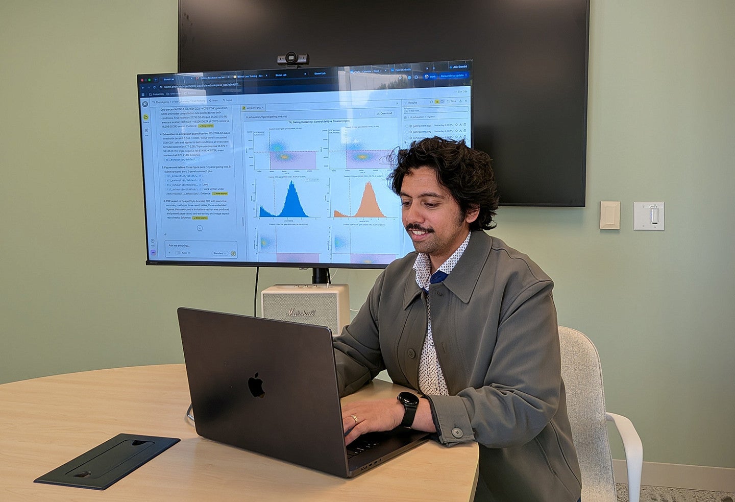 man sitting at laptop at conference table with graphs on screen behind him