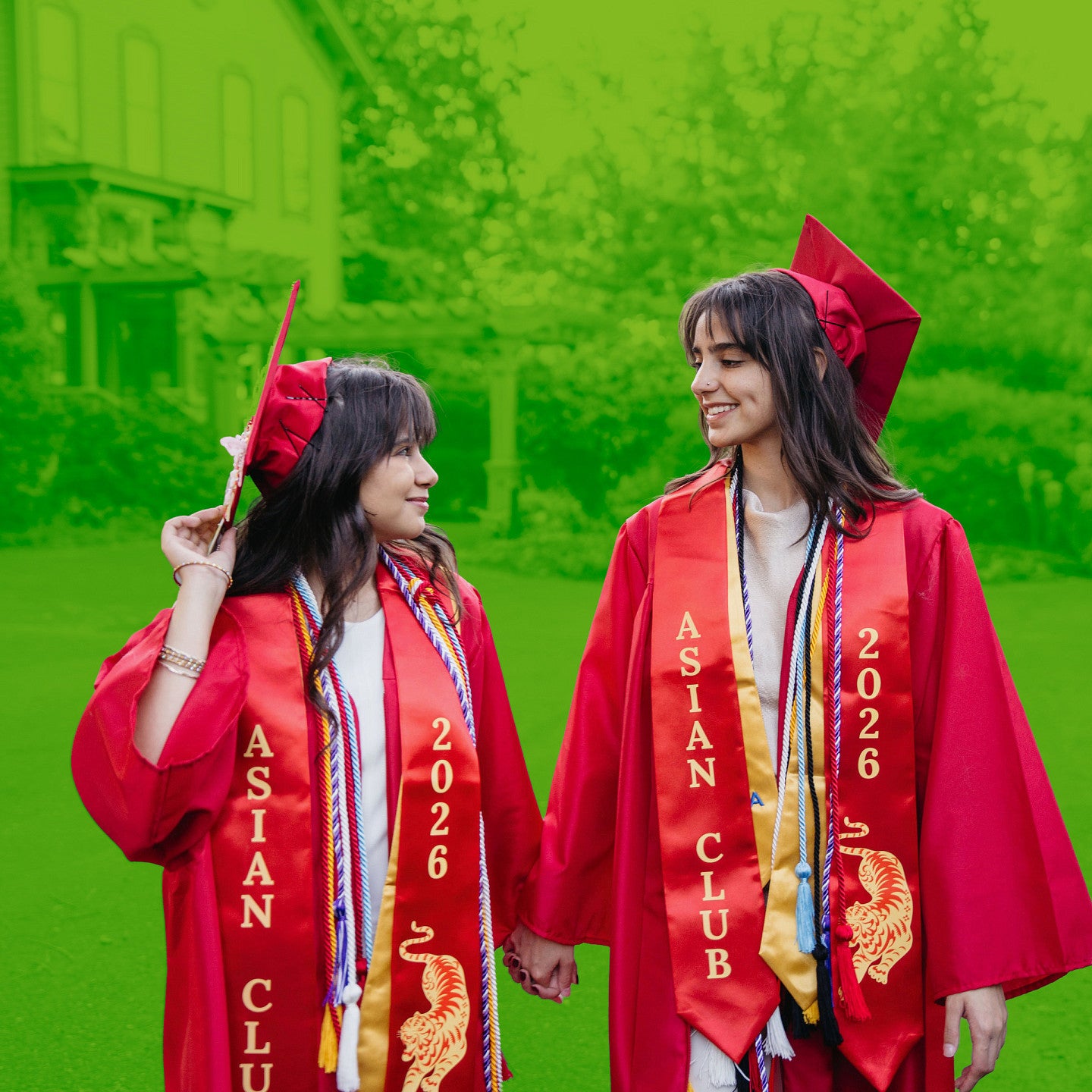 twin sisters posing hand in hand in red graduation cap and gowns, with green duotone background of old house on country landscape