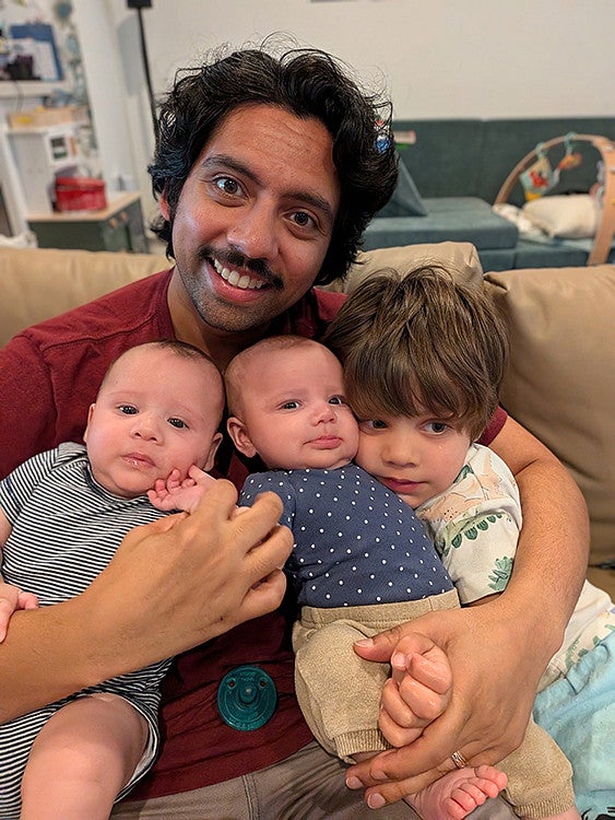 father with three small children in arms on couch, smiling