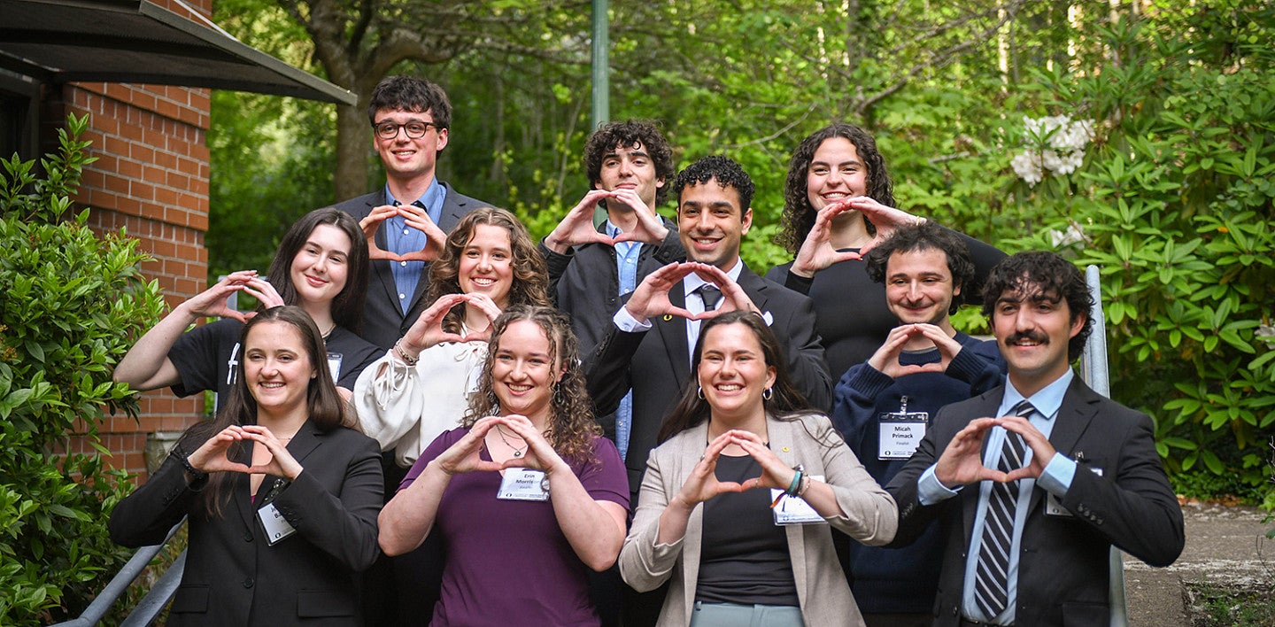 11 student finalists in the 2026 three minute competition, posing outside on campus and throwing the O