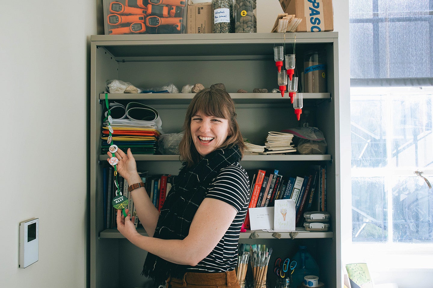 kristen Rahilly posing with items on her office shelves representing past projects with students