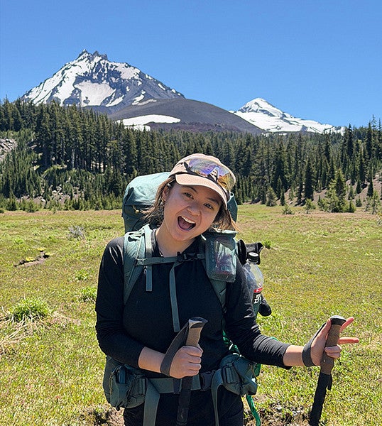 person backpacking through alpine meadow and posing in front of snowcovered peaks