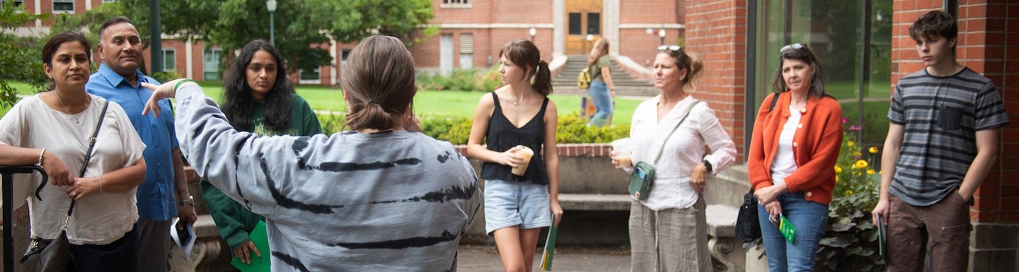 A group of prospective students and family standing outside chapman hall, facing a tour guide who is gesturing