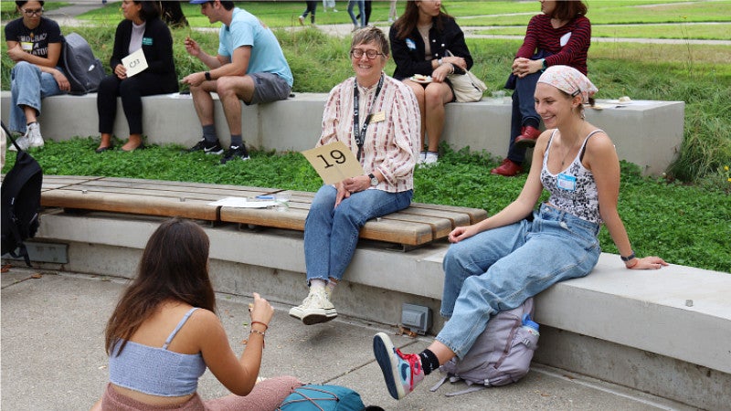 Professor Carol Stabile sits with a group of students on the edge of Tykeson-Chapman lawn