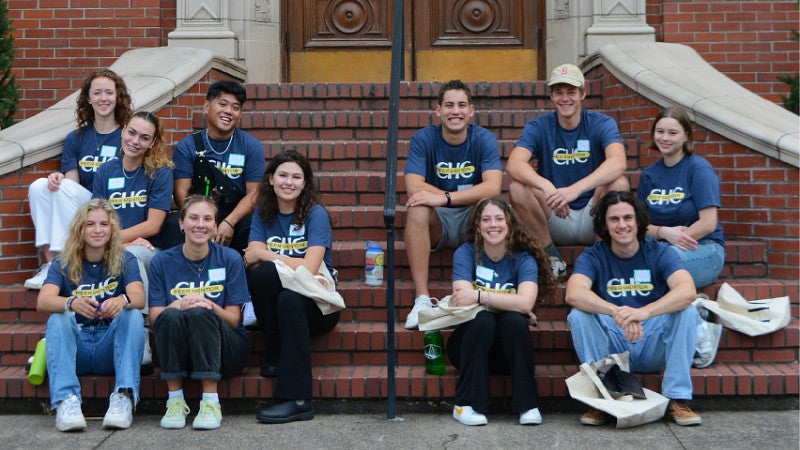 A group of first-year students wearing blue shirts sits on brick steps.