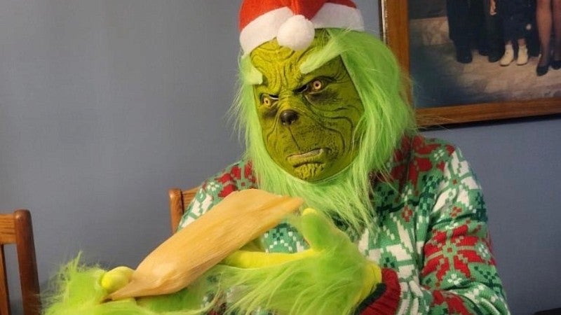 a person dressed as the grinch who stole christmas eating a plate of tamales