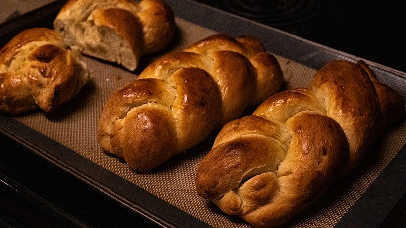 freshly baked, golden brown braided dinner rolls on a sheet pan cooling on a stovetop