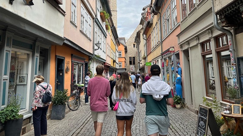 group of students walking down a narrow pedestrian cobblestone street with european buildings