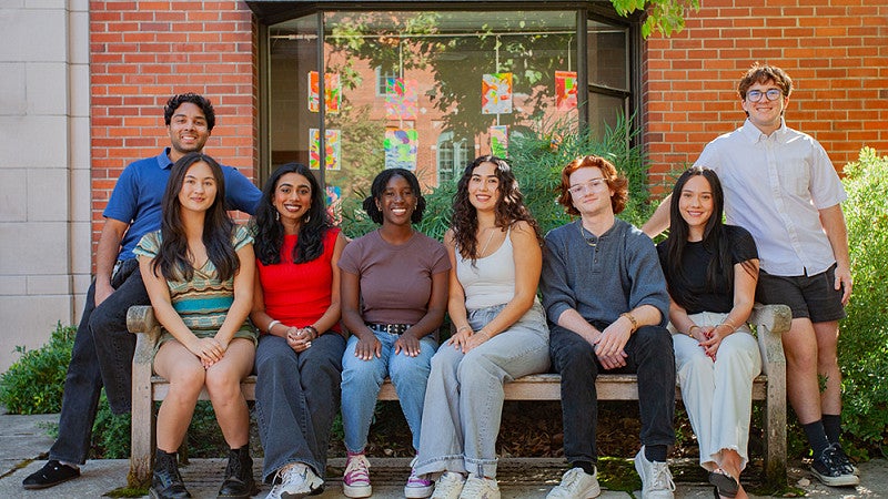 group of students seated on and standing around a bench outside Chapman Hall