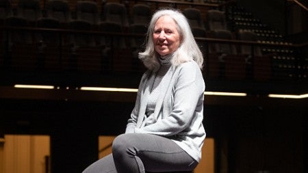 Ginerva Ralph seated on a spot-lit stage.