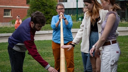 lydia van dreel playing the alpenhorn on tykeson lawn with students looking on