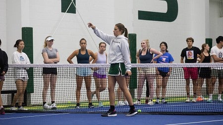 ruby wool speaking to a group of tennis players on an indoor court