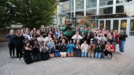 group of students clustered around the duck statue on UO campus, throwing the O