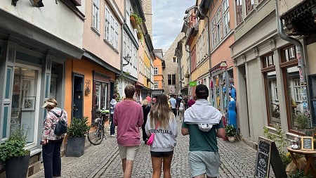 group of students walking down a narrow pedestrian cobblestone street with european buildings
