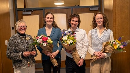 winners of the three minute thesis competition posing with dean carol stabile, holding bouquets