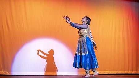 gayatri misra performing a traditional indian dance on stage in front of orange background