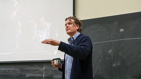 chc professor casey shoop teaching at front of classroom with thermos in hand