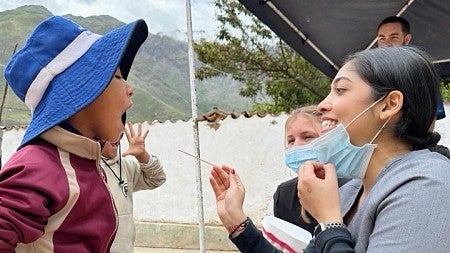 people under tent with mountainous landscape: person in medical scrubs and mask swabbing the throat of a boy