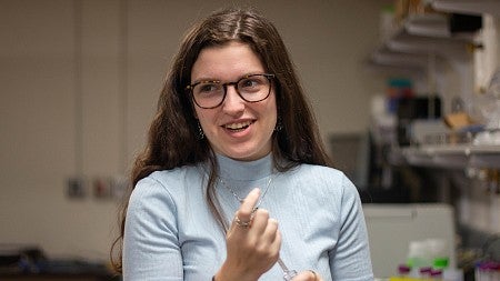 student in lab holding pipette, smiling off camera