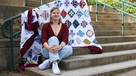 portrait of student sitting on amphitheater steps with colorful quilt draped on railing behind her