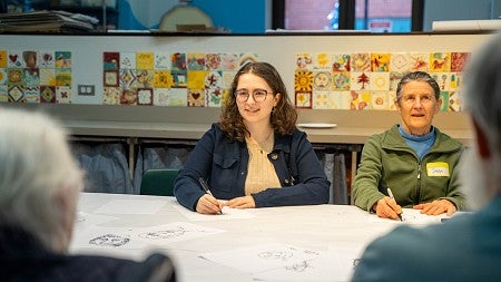 olivia black seated at a table in a classroom with senior-aged students and art decorating the walls