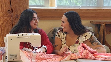 two people smiling together seated at a sewing machine