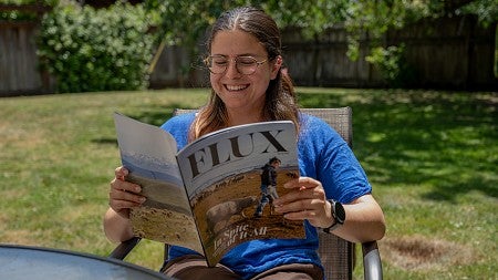 person sitting at backyard table looking through flux magazine and smiling
