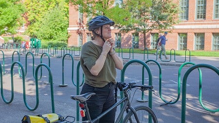 larissa stiglich buckling on her helmet standing at bike on campus