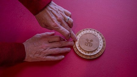 hands using a wooden cipher wheel on a red table