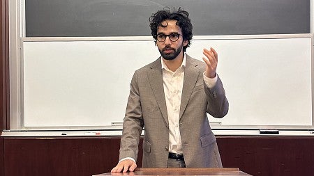 parsa aghel standing at a lecture hall podium, speaking and gesturing