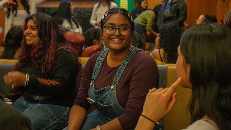 student smiling at another student in a crowded, lively room of students engaging with one another