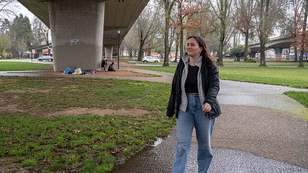 person walking through a park under a highway on a rainy day