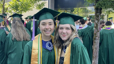 two students at commencement in green caps and gowns