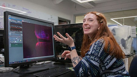 avery suriano laughing while seated at lab computer with colorful science image on screen