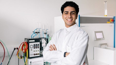 student posing in research lab in white lab coat