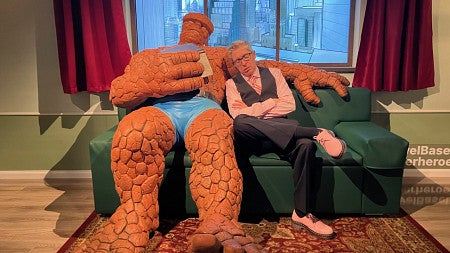ben saunders pretending to sleep on a couch next to a life-sized marvel character figure