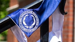 blue and white honors college graduation stole draped on railing outside chapman hall on sunny day