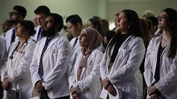 medical students in white coats standing at an initiation ceremony, reciting an oath